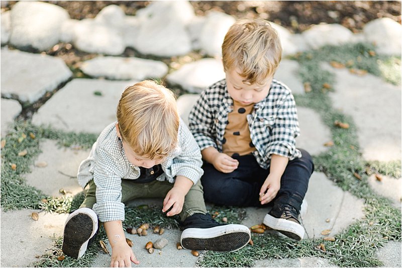 Overhead shot of 2 year old twin brothers sitting on flagstone playing with acorns during their family photo session in Pasadena, CA.