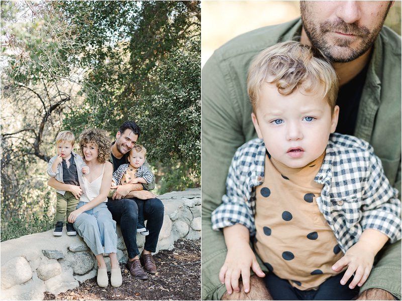 Image on the left shows parents sitting on a grey stone wall holding their 2 year old identical twin sons surrounded by oak trees.  Image on the right shows twin wearing brown tshirt with black polka dots with a black and cream checkered button down layered on top, as he sits on his father's lap.