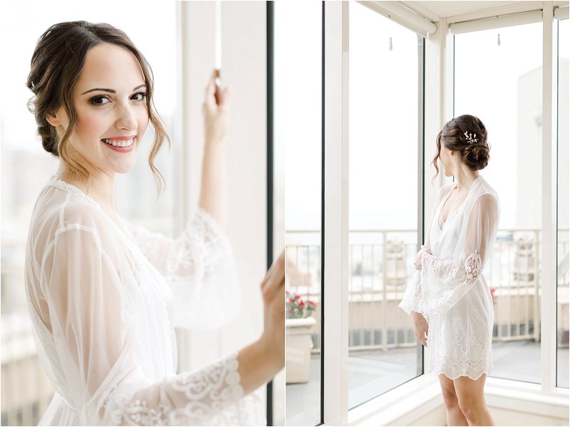 Image shows brunette bride who chose the perfect getting ready location, standing in front of full length windows with luminous natural light surrounding her.  