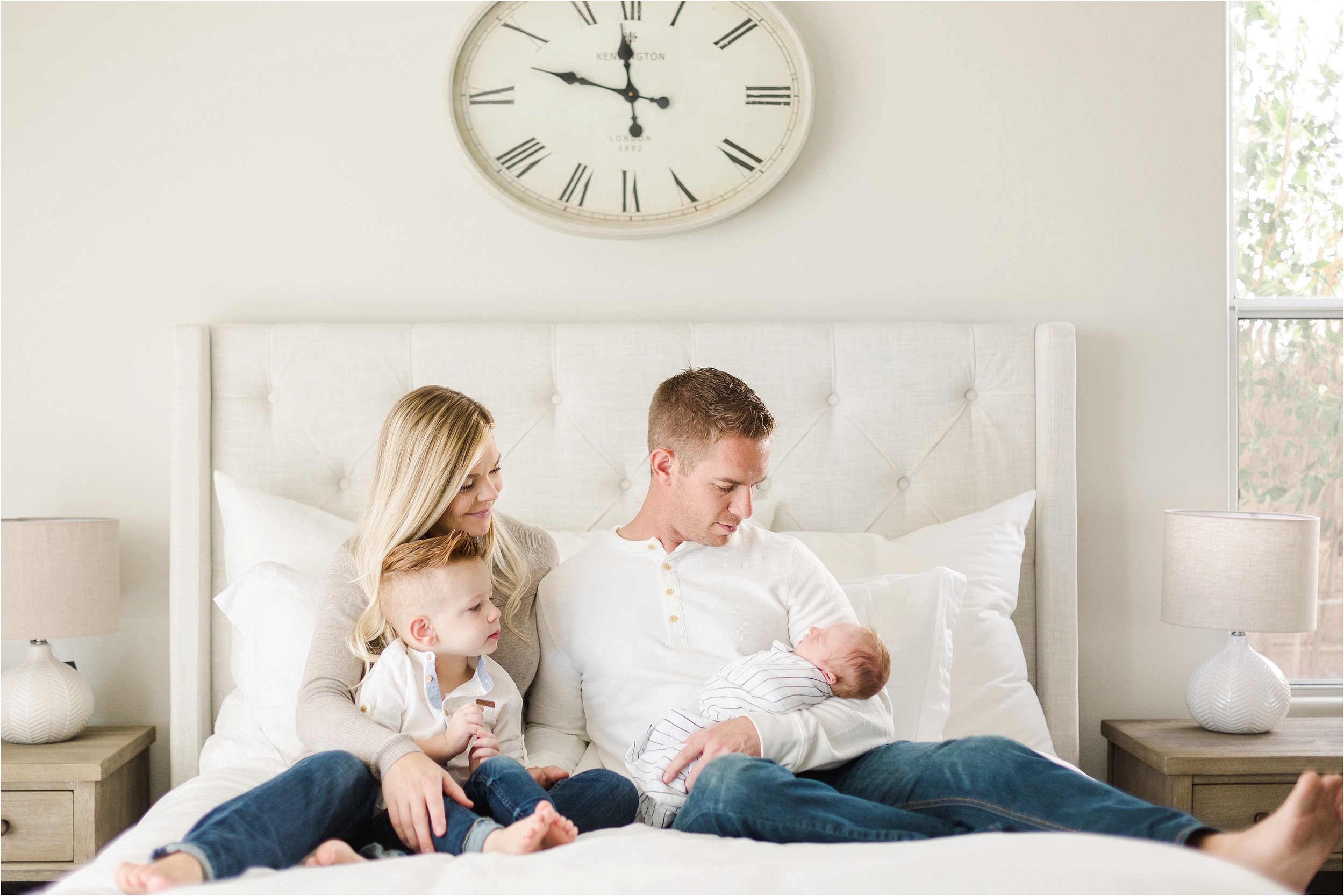 Family of 4 snuggles on the bed during their at home newborn photoshoot.