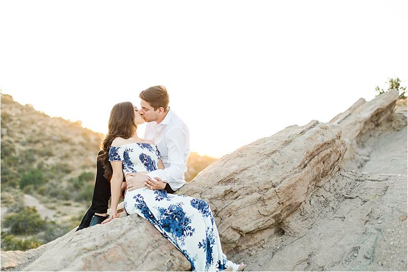 Fiances share a kiss during golden hour as they sit on a rock formation at Vasquez Rocks, CA during their engagement session.