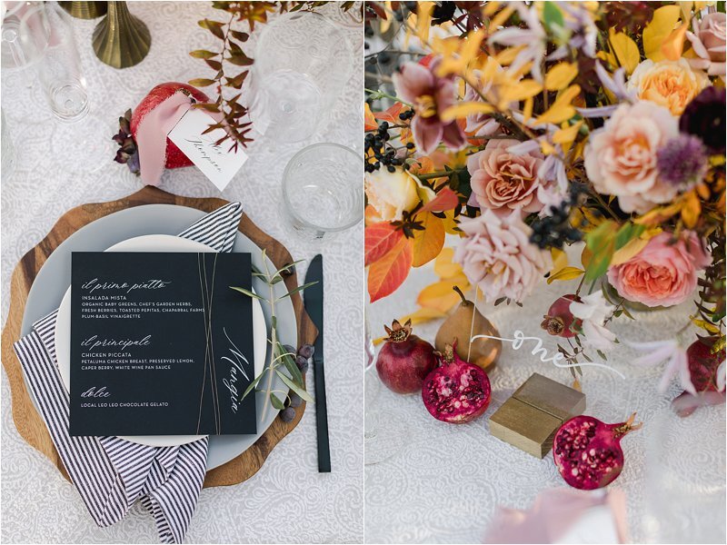 Vibrant fall wedding tablescape featuring white lace tablecloth, bright florals of yellow, orange, pink and purple flowers, bosc pears and pomegranets, wood chargers, grey dinner plate, striped napkin, white salad plate, black menu, black flatware and acrylic table numbers with gold base.