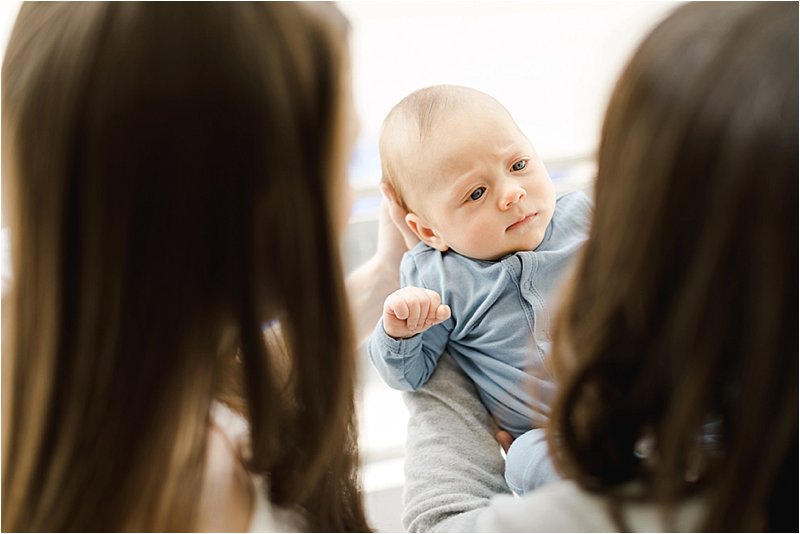 Baby boy's face is seen between his mother's heads as he looks up at them.