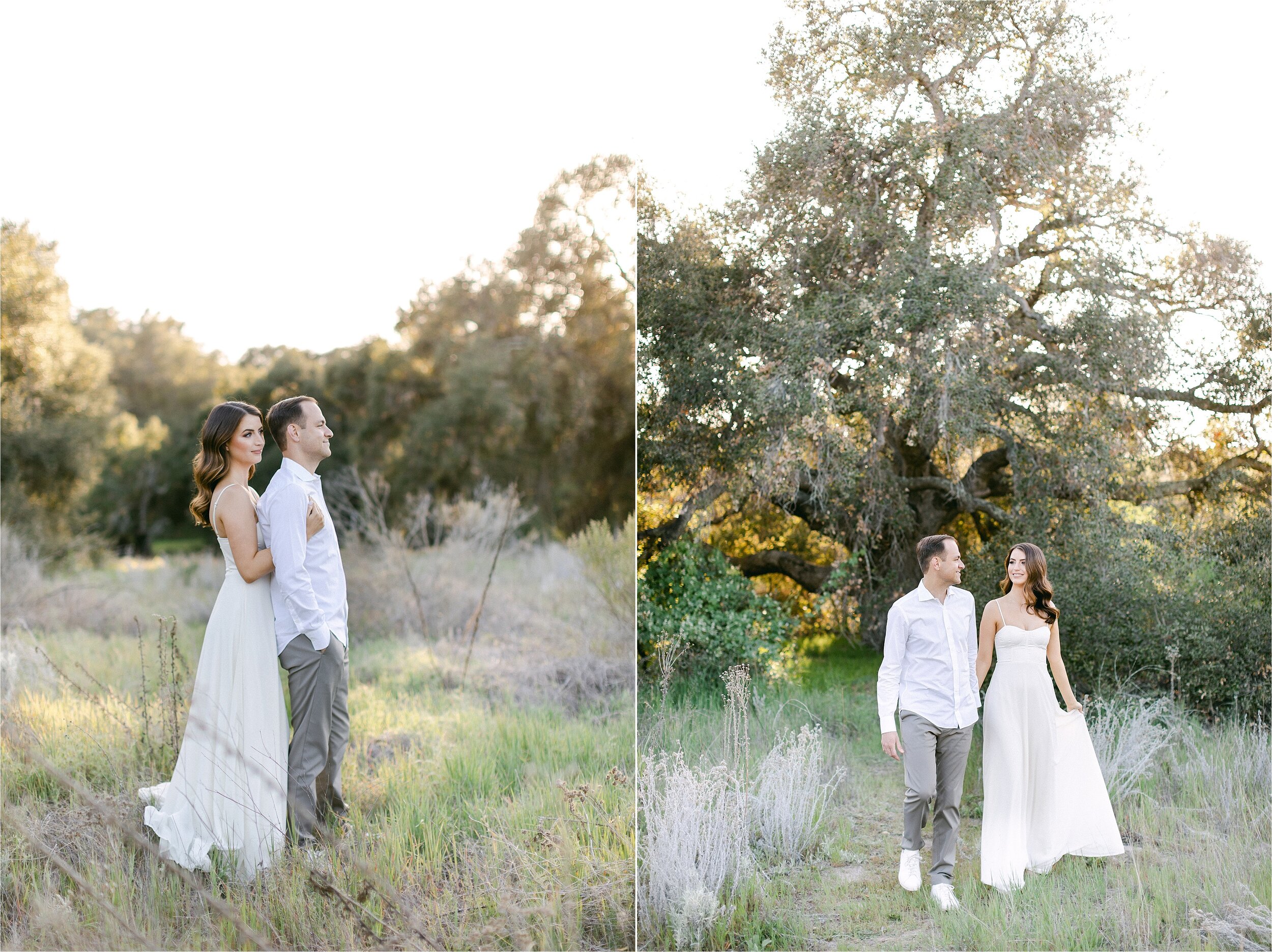 Bride-to-be in white chiffon gown embraces husband from behind as they stare off into the distance in an open field during their engagement photography session in Orange County, CA.