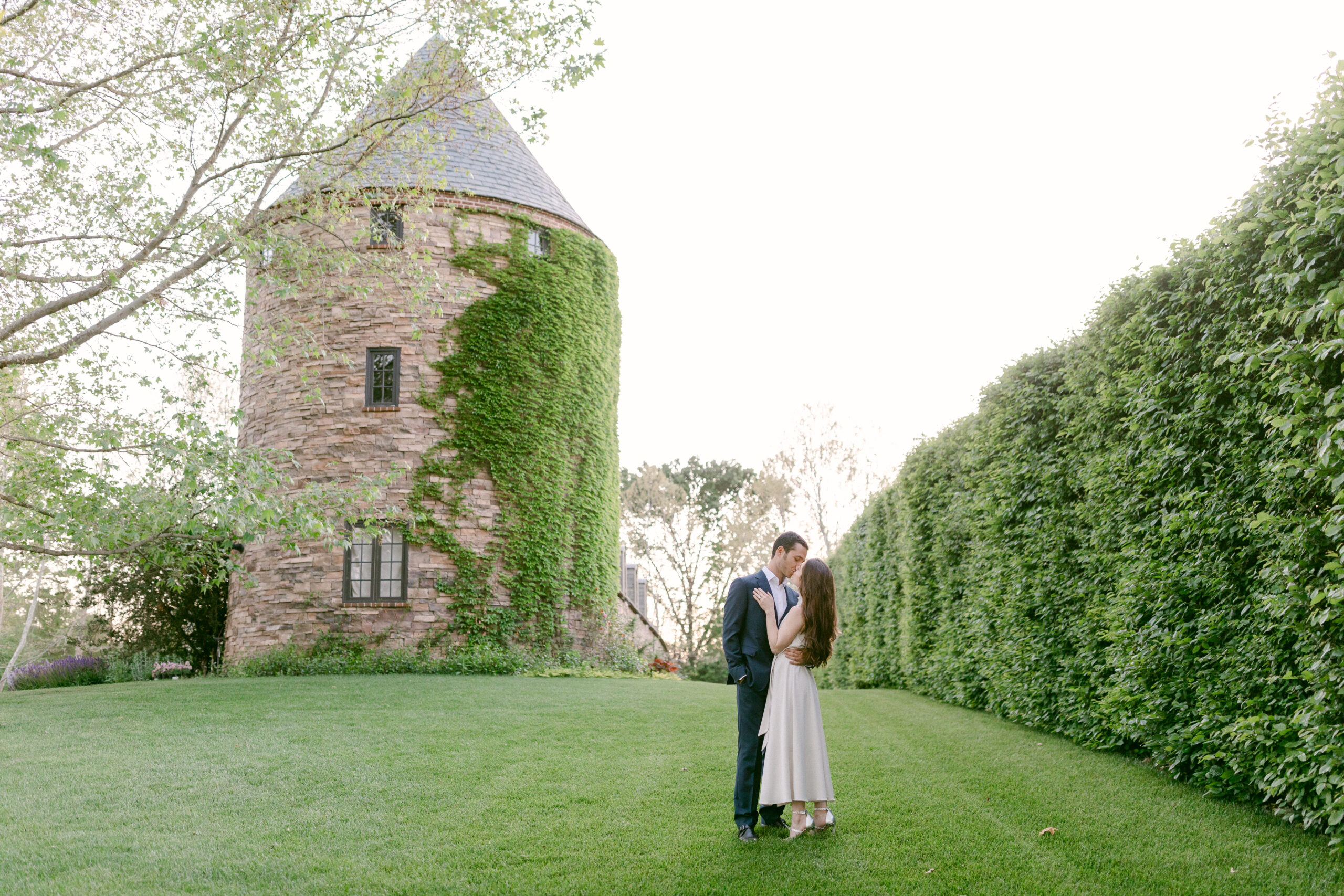 Bride and Groom to be embrace on a lush lawn in front of a beautiful French dovecote at Kestrel Park during their engagement session with Santa Ynez Wedding Photographer, Tiffany J Photography