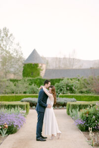 Images taken by Santa Ynez Wedding Photographer, Tiffany J Photography, show Bride and Groom to be embrace in the center of the lush garden at Kestrel Park with the Dovecote behind them.