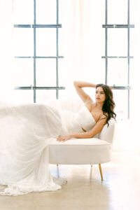 Brunette bride is delicately draped over a white sofa with her hand in her hair while posing for an editorial wedding photo shoot in downtown Los Angeles.