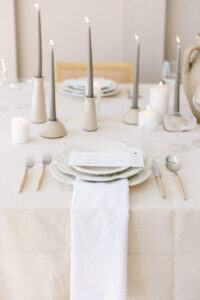 Wedding reception tablescape featuring cream linen tablecloth, cream dishes, and taupe candles.