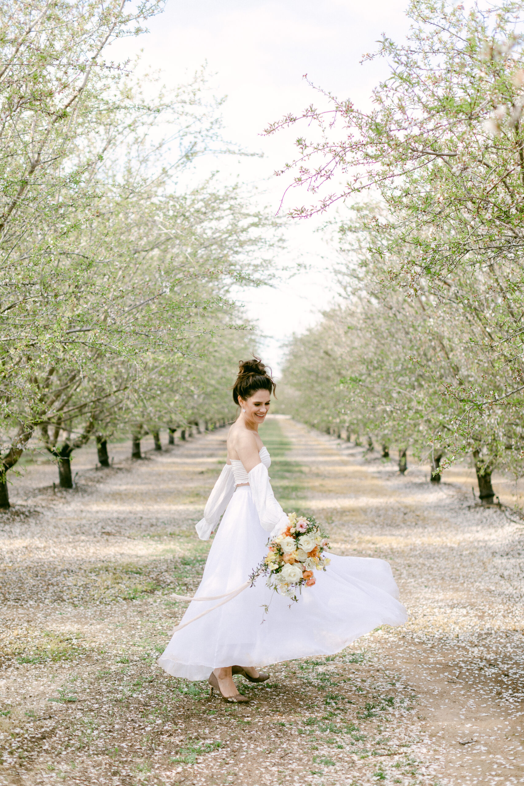 Bride twirling in almond blossom orchard while holding bouquet