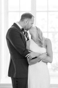 Black and white photo of bride and groom embracing and sharing a kiss.