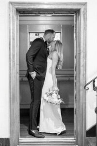Black and white photo of bride and groom sharing a kiss in the elevator.