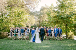 Horizontal image shows the back of the bride's dress as she walks down the aisle, escorted by both her Mother and Father.