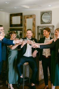 Groom sits on a barstool as he and his "grooms-people" (men and women) share a toast.