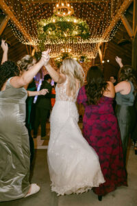 The bride and her best friends hold hands and charge the dance floor to celebrate her marriage with her.