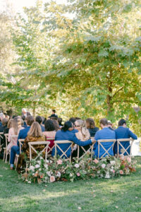 Photo shows guest seated as the wedding ceremony is about to start.  One couple shares a kiss.