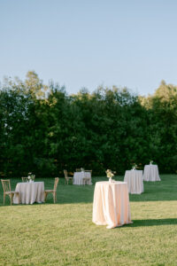 Both high and low tables with light pink table cloths scattered across the lawn for cocktail hour.