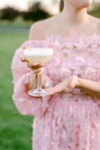 Female guest in a beautiful pink, off the shoulder dress, showcases one of the craft cocktails made by Flair Project.