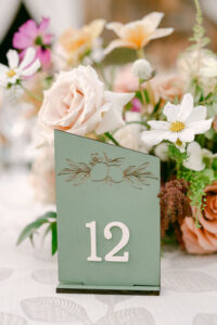 Detail photo of the custom sage green reception table numbers with white numbers, and a gold, de-bossed design on the top.