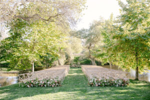 Beautiful lakeside wedding ceremony with light wooden crossback chairs, and pink floral arrangements. 