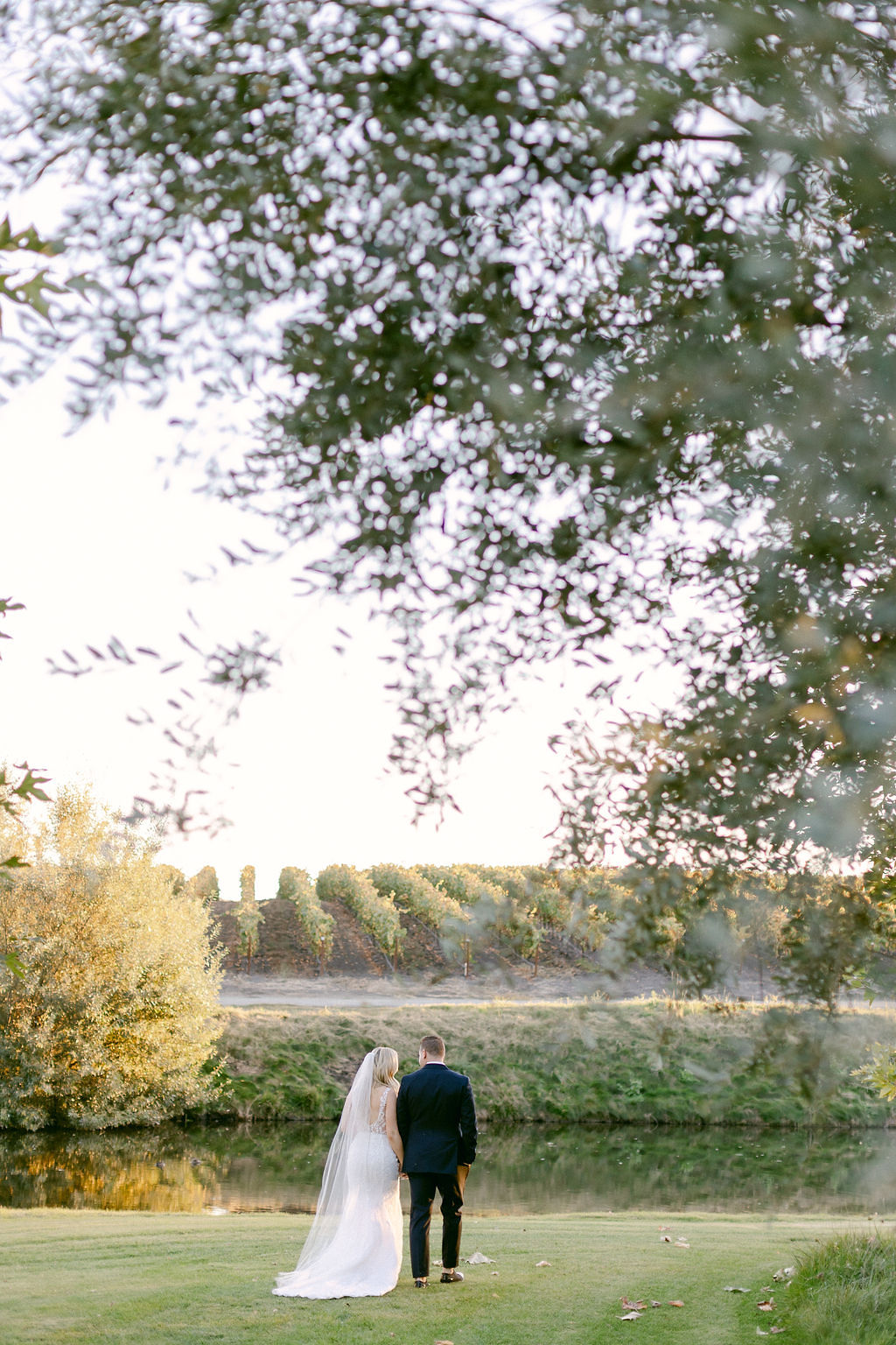 Bride and groom take a walk across the lawn toward the lake following their wedding ceremony