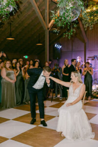 Groom kisses Bride's hand as she sits on a chair at the beginning of their first dance as husband and wife.