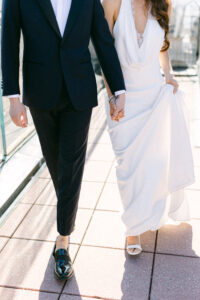 Fashion forward bride and groom walk hand in hand following their wedding at Top of the Rock