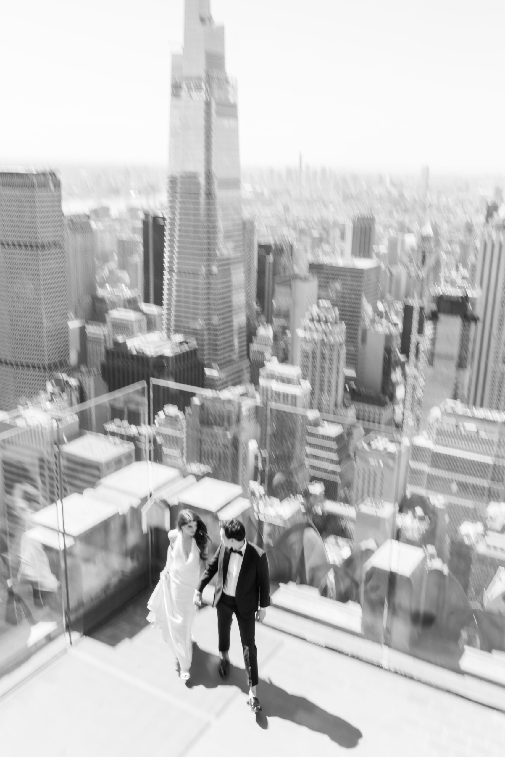 Black and white, motion blur image of bride and groom walking hand in hand with the NYC skyline in the background