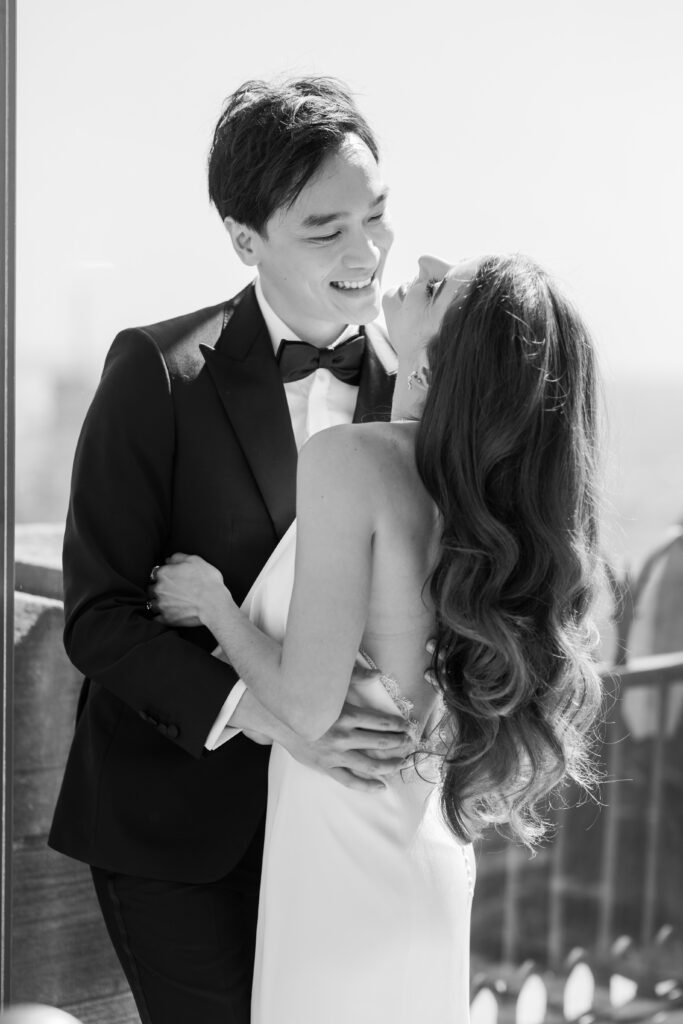 Romantic, candid, black and white image of bride and groom embracing as she throws her head back and laughs while groom looks adoringly at her.