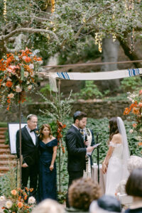 Grooms parents watch as their son exchanges vows with his wife to be during their outdoor wedding ceremony under the oak trees at Calamigos Ranch.