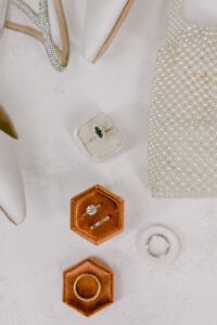 Close up of bridal flatlay showcasing her wedding rings, pearl clutch and shoes.