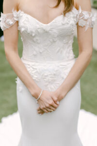 Detail photo of bride's fit to flare Suzanne Neville "Romance" gown, with a sweetheart neckline, off the shoulder cap sleeves, and delicate floral applique scattered over the bodice.