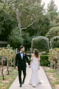 Bride and groom hold hands as they walk through the vineyards at Calamigos Ranch on their wedding day.