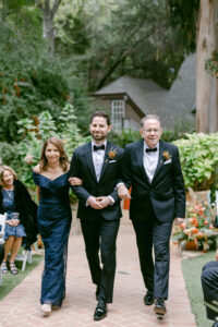 Groom walks down the aisle with his parents escorting him on his wedding day.