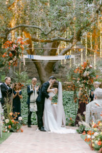 Bride and groom share their first kiss as husband and wife at the conclusion of their wedding ceremony, under the oak trees at Calamigos Ranch during their fall themed wedding.