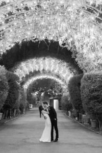 Black and white photo of bride and groom kissing under a beautifully lit archway at Calamigos Ranch.