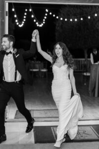 Black and white photo of bride and groom cheering as they enter the ballroom for their first dance.