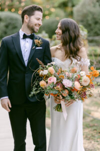 Bride and groom hold hands and smile at each other.