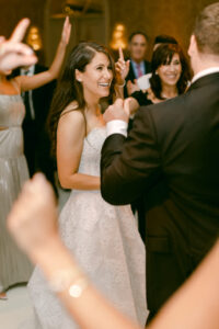 Bride smiles and laughs as she and her new husband are surrounded on the dance floor by their friends and family.