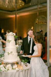 Bride playfully smudges frosting on groom's nose as they cut their wedding cake.