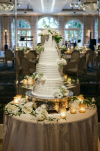 Beautiful 4 tiered white wedding cake decorated with white flowers and surrounded by candles.