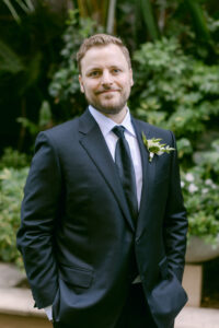 Portrait of groom wearing black tux and tie in the lush courtyard of the Four Seasons Beverly Hills.