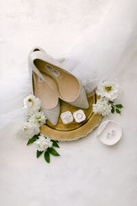 Bridal detail flatlay showcasing sparkly Jimmy Choo heels, wedding rings, and bride's diamond earrings.