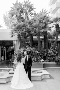 Black and white photo of bride and groom standing in front of the fountain in the courtyard of the Four Seasons of Beverly Hills with Palm Trees behind them.