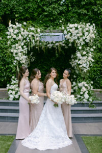 Portrait of bride and her 3 bridesmaids in front of her white rose chuppah, in the lush green courtyard of the Four Seasons Beverly Hills. 