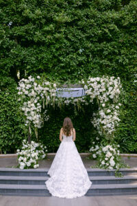 Bride stands on the stairs in front of her chuppah, showcasing the back of her strapless, lace, Monique Lhuillier gown at the Four Seasons Beverly Hills. Photographed by SoCal wedding photographer Tiffany J Photography.