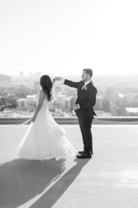 Black and white photo of bride spinning as she and her groom hold hands on the rooftop of the Four Seasons Beverly Hills as the sun sets in the background.