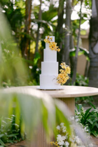 A wedding cake on a table, elegantly displayed amidst lush palm trees in a tropical setting.