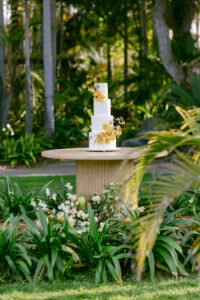 A wedding cake on a table, elegantly displayed amidst a serene backdrop of lush green trees.