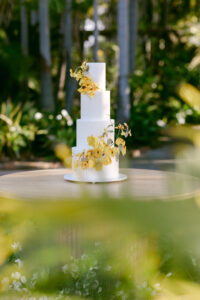 A yellow-themed wedding cake on a table, surrounded by trees, set in a spring outdoor wedding venue.