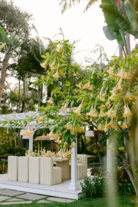 A yellow themed micro-wedding tablescape, surrounded by striped yellow upholstered chairs under a gazebo in a garden setting.